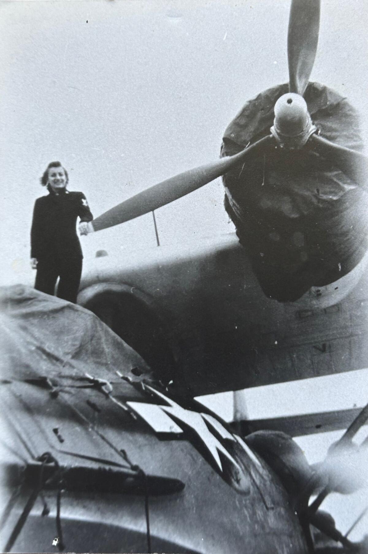 A young woman stands next to the propeller of a large plane.
