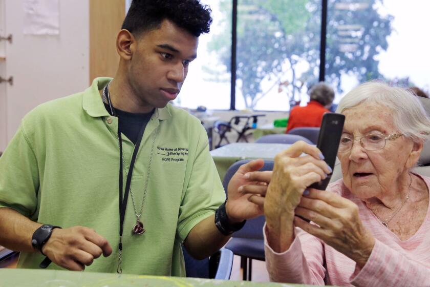 Kevin Perez, 19, in the HOPE program at the Hebrew Home at Riverdale, in New York, assists resident Belle Bishop, age 93, with her mobile phone in the art studio Thursday, May 25, 2017. The nursing home on a picturesque stretch of the Hudson River in the Bronx, has gone beyond its calling as a house for the old, playing host to the young with an innovative public high school right within its walls. (AP Photo/Richard Drew)