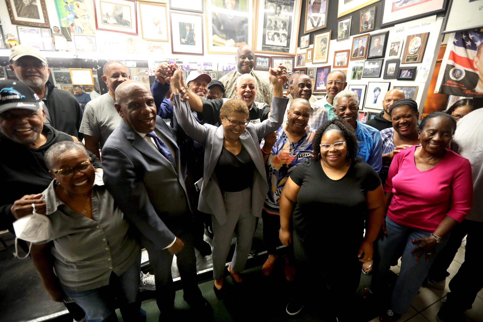 Supporters raise Karen Bass' hands over her head as others surround her in a room covered in portraits and other art.