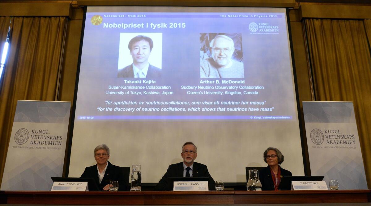 Portraits of Takaaki Kajita, left, and Arthur B. McDonald are projected behind Nobel Committee for Physics members at a news conference about the two prizewinners.