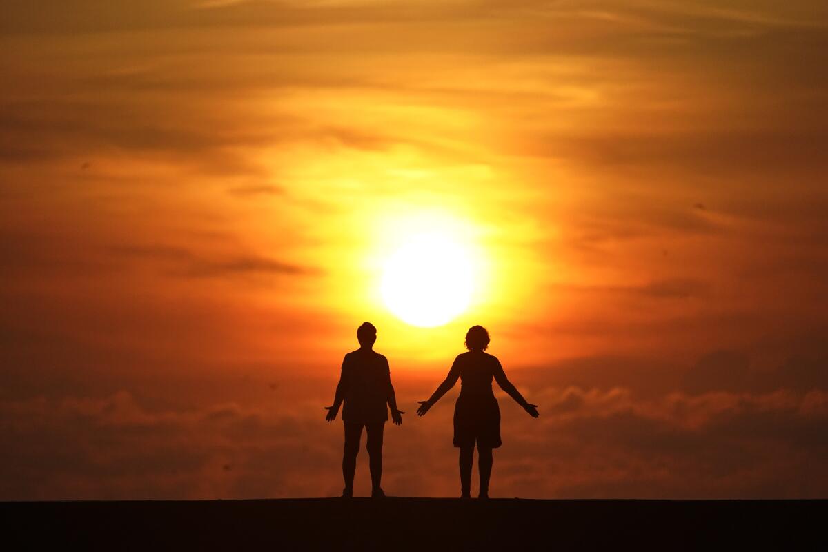 Two people stand on a jetty as the sun rises over the Atlantic Ocean.