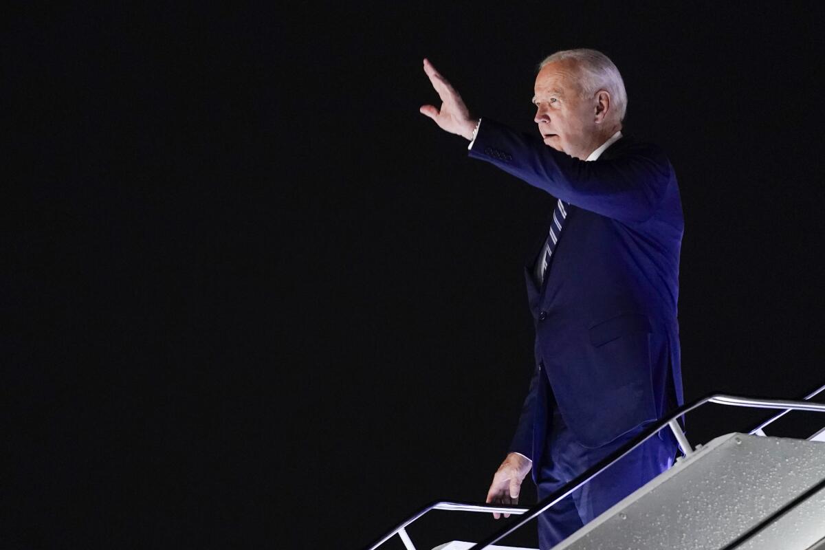 President Biden waves as he descends the stairs on Air Force One at night 