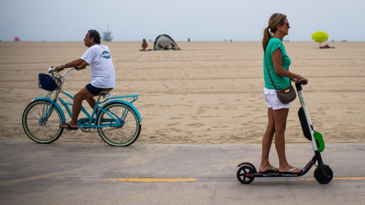 A Lime electric scooter rider passes a cyclist on the Venice Beach Boardwalk in Venice on July 25, 2018.