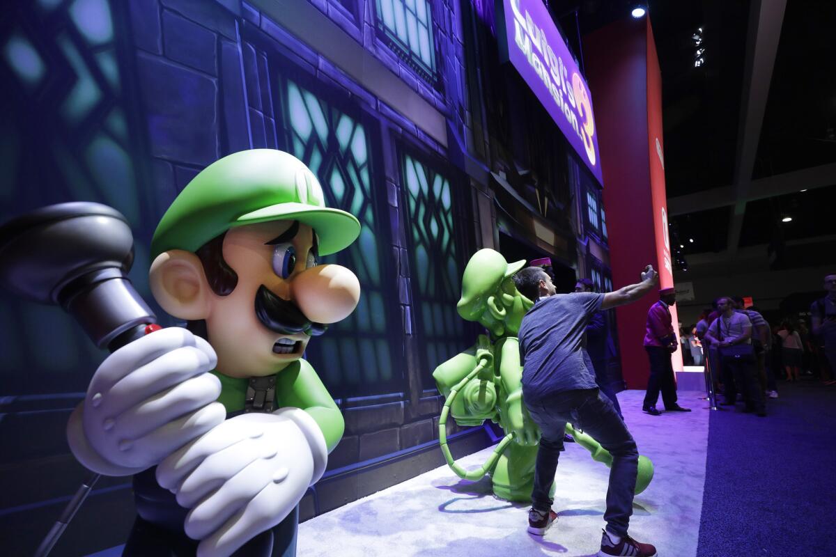 An E3 attendee takes a selfie in front of "Luigi's Mansion 3" at the Los Angeles Convention Center.