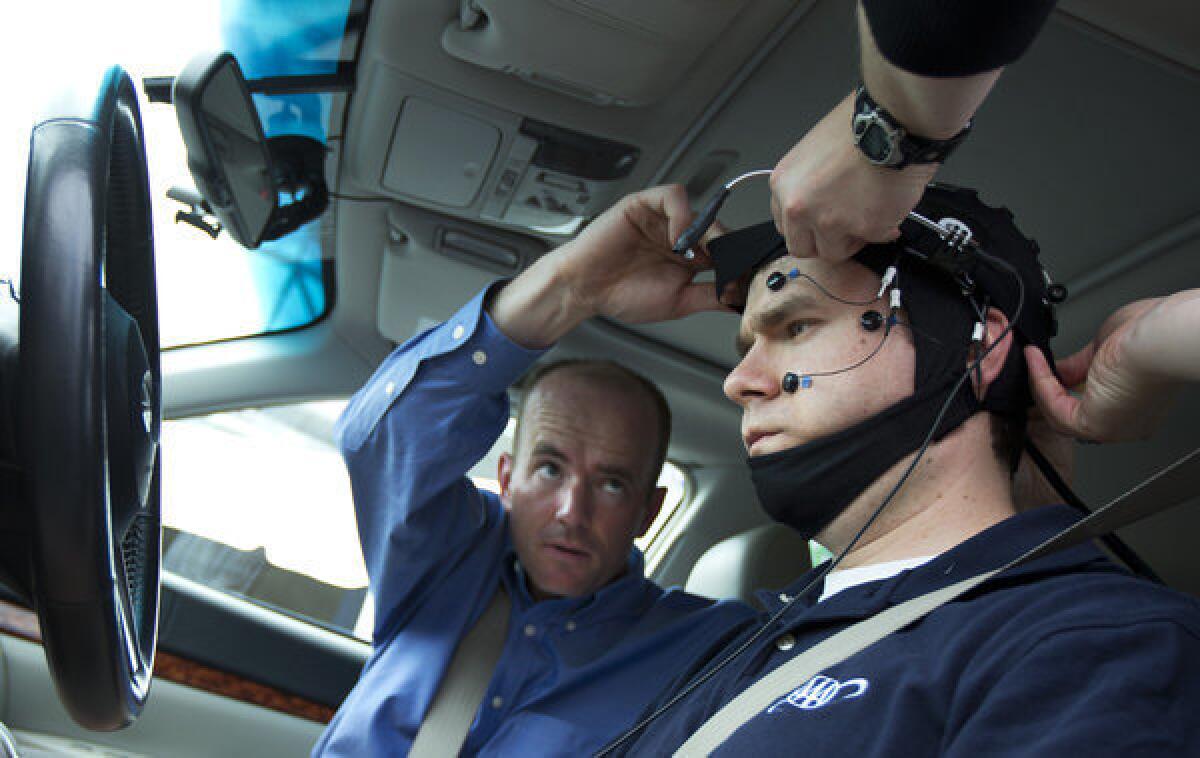 Russ Martin of AAA is assisted by Joel Cooper, left, in hooking up the electroencephalographic-configured skull cap to the research vehicle during a demonstration in support of their new study on distracted driving.
