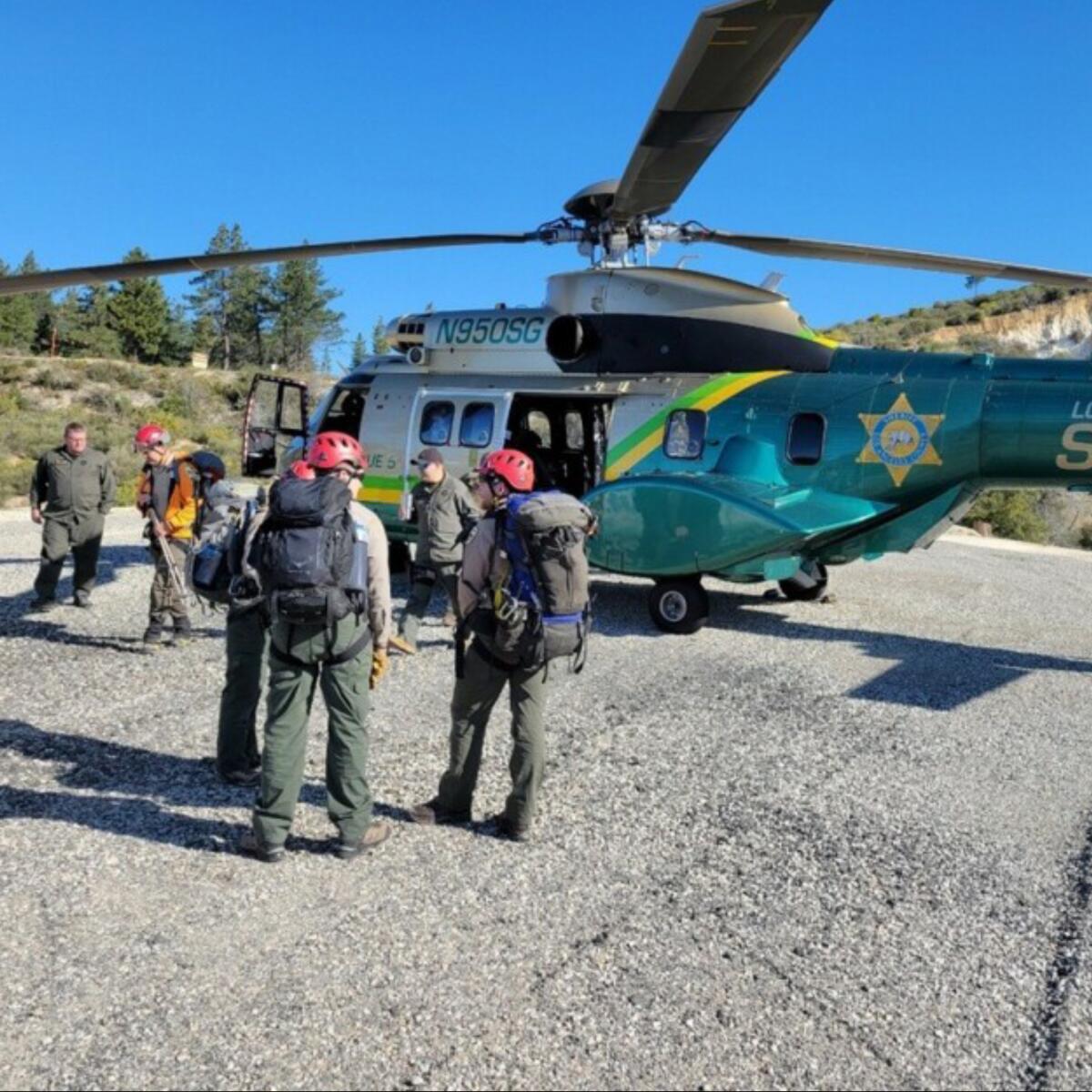 Search teams stand in front of a helicopter.