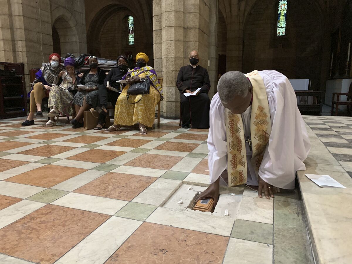 In this photo provided by Oryx Media, Anglican Archbishop Thabo Makgoba lays the ashes of Archbishop Emeritus Desmond Tutu to rest at the high altar of St. George's Cathedral, in Cape Town, South Africa. Sunday. Jan 2, 2022. Tutu died on Dec. 26, at age 90. At back are members of the Tutu family and Dean Michael Weeder of the Cathedral. (Benny Gool/Oryx Media via AP)