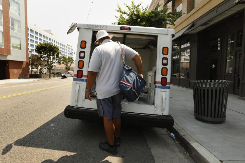 San Pedro, California,-Aug. 20, 2020-A Los Angeles county postal carrier delivers mail on Aug. 20, 2020. United States Postal Workers were offered 12 weeks leave due to the coronavirus pandemic, which caused a backlog of mail that needed to be delivered. Many postal carriers were offered overtime. A lack of enough postal carriers is one of the reasons that the United States Postal Service is behind on delivering mail. (Carolyn Cole/Los Angeles Times)
