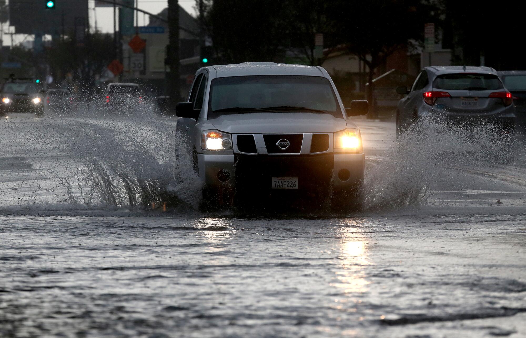 An SUV goes through a flooded part of a road, splashing water.