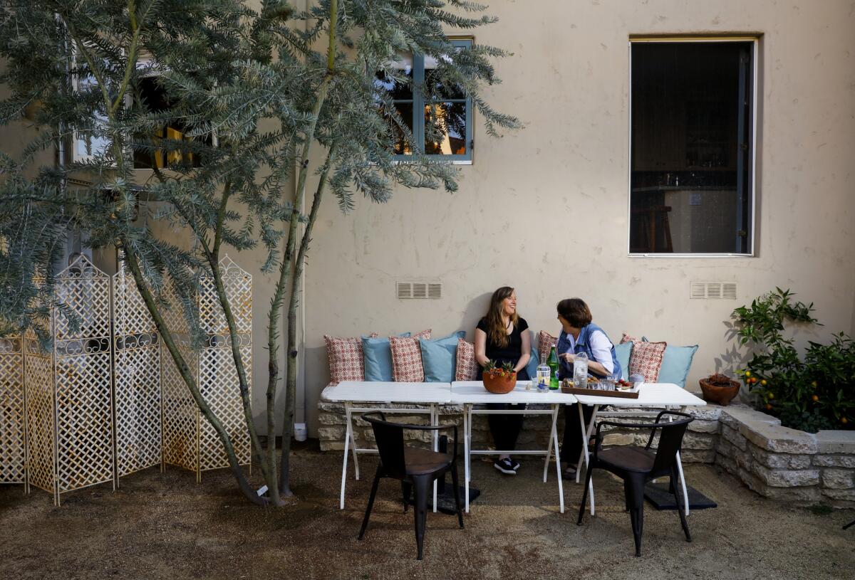 Designer Margaret Oakley Otto, left, and homeowner Sarah Olsen relax on a banquette made of broken concrete. The three-bedroom, two-bath home was moved from Miracle Mile to Manhattan Beach during the 1950s and was elevated on pylons, causing the home to feel detached from the yard.