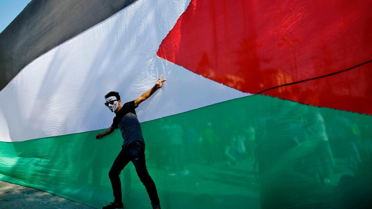 A Palestinian youth celebrates in front of the Palestinian flag in Gaza City after rival factions Hamas and Fatah reached a preliminary agreement on ending a decade-long split on Oct. 12, 2017.