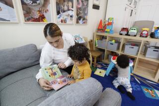 Lakewood, CA - May 17: Jennifer Cortez, childcare assistant, reads to Enzo Muniz, 20-months-old, while Luca Brown, 8 months old, plays at right, at Zoila Carolina Toma's family childcare center in Lakewood Wednesday, May 17, 2023. Zoila is licensed to care for up to 14 children from 8 months-12 years old Inside her center. They have a nap room, an art area, and a reading area to promote a comfortable atmosphere where students can engage in their activities. Currently, Zoila is at capacity, but she is constantly receiving calls from families looking for high-quality care. The need for care is desperately there, but there are not enough family child care centers to cover the needs of families, and few want to enter an industry where wages are so low. (Allen J. Schaben / Los Angeles Times)