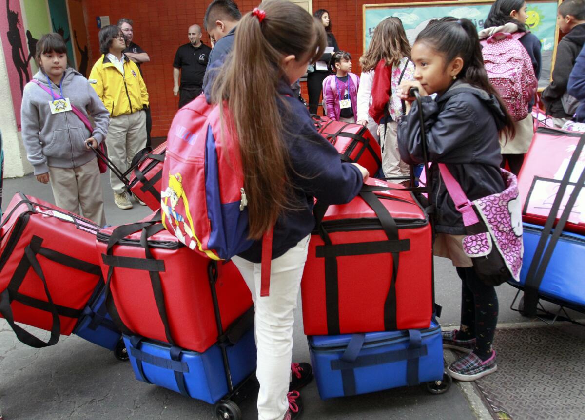 Mayerly Tejano, 7, right, leans on a container that keeps food warm while she chats with her friends at Figueroa Street Elementary School as they prepare to deliver food for a classroom breakfast program.