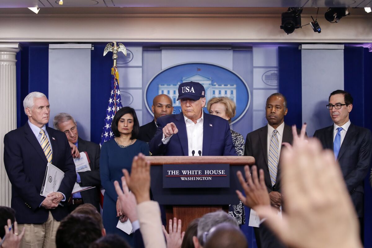 President Trump, wearing blue "USA" cap, at a lectern with Mike Pence and others in front of reporters.