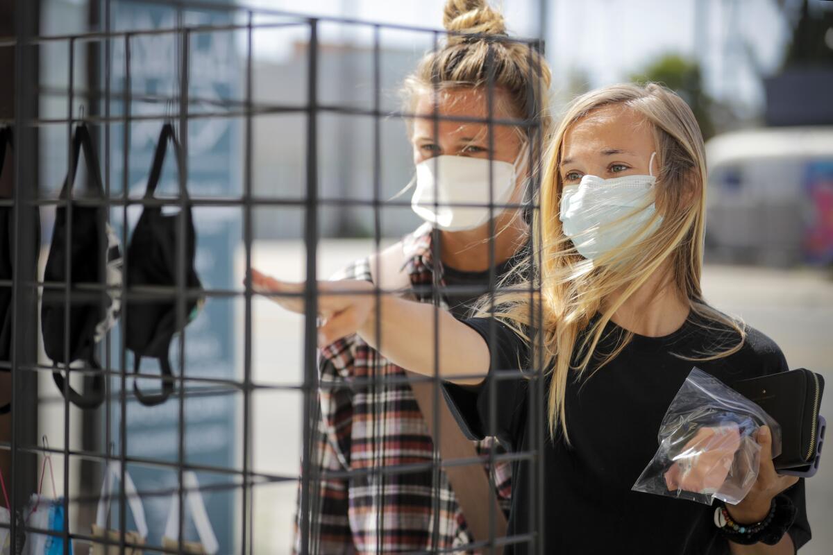 Sisters Haley Grawe, left, and Aubrey shop for face masks at a stand in front of Amiga Wild in Venice.
