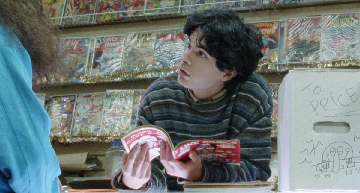 A person stands at a counter looking at a magazine. Shelves behind him are filled with comic books in plastic covers.