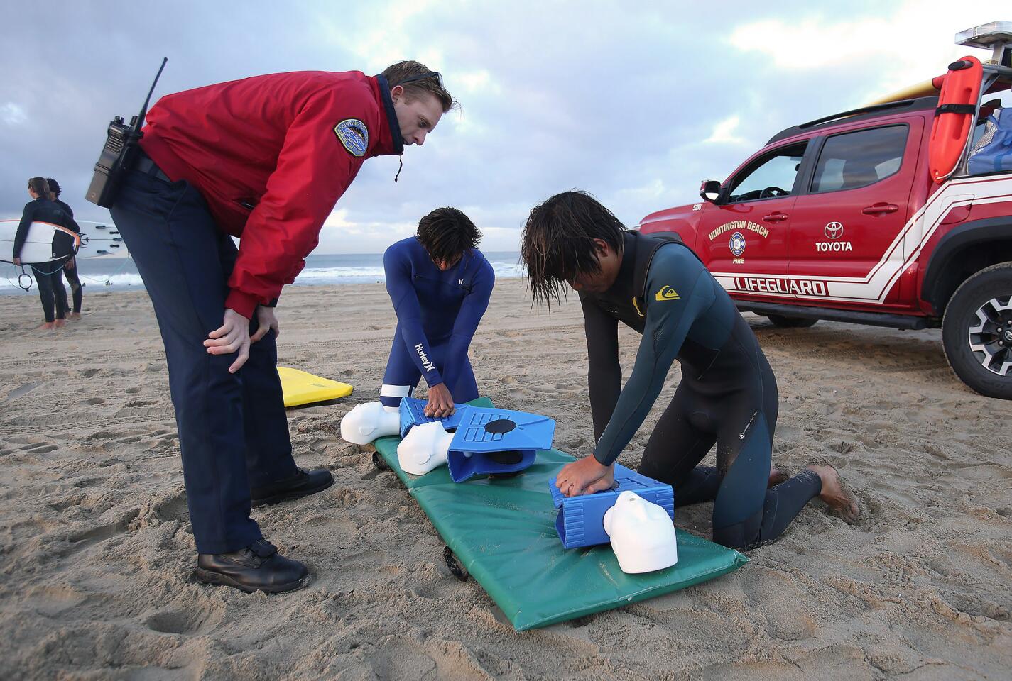 Huntington Beach marine safety officer Sterling Foxcroft teaches Huntington Beach High School students Sage Guinaleo, center, and Keanu Igarashi proper chest compression methods during a session Wednesday to train members of the school surf team in lifesaving techniques.