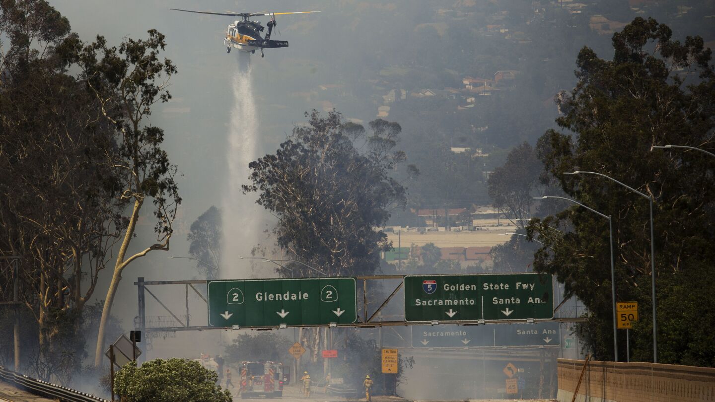 A helicopter drops water while firefighters work to control a blaze that threatened structures along the 2 Freeway where it meets the 5 Freeway.