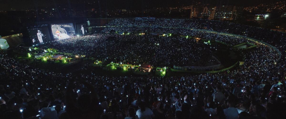 A stadium is packed with people holding up their cellphone lights.
