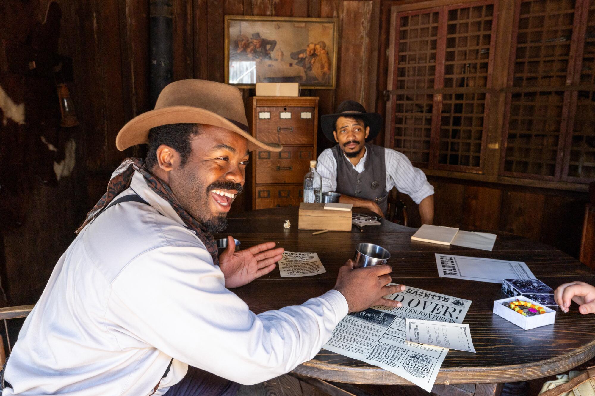 Two men in western-style period clothing sitting around a table.