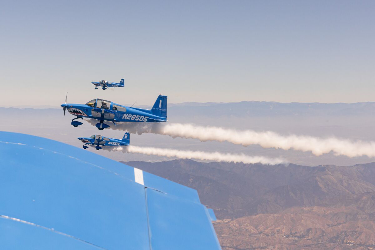 Three blue planes fly close together and leave a trail of smoke in the air near a mountain range.