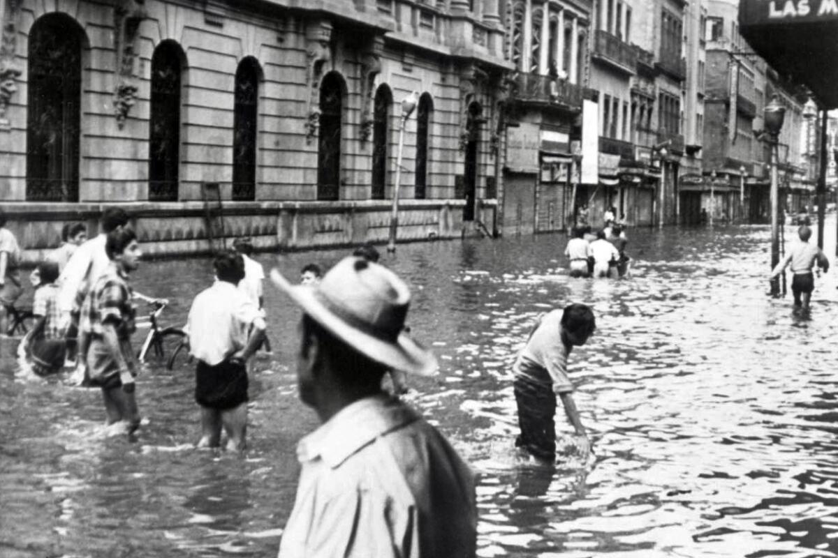 墨西哥城街道上，人们在齐膝深的水中行走的档案照片。 