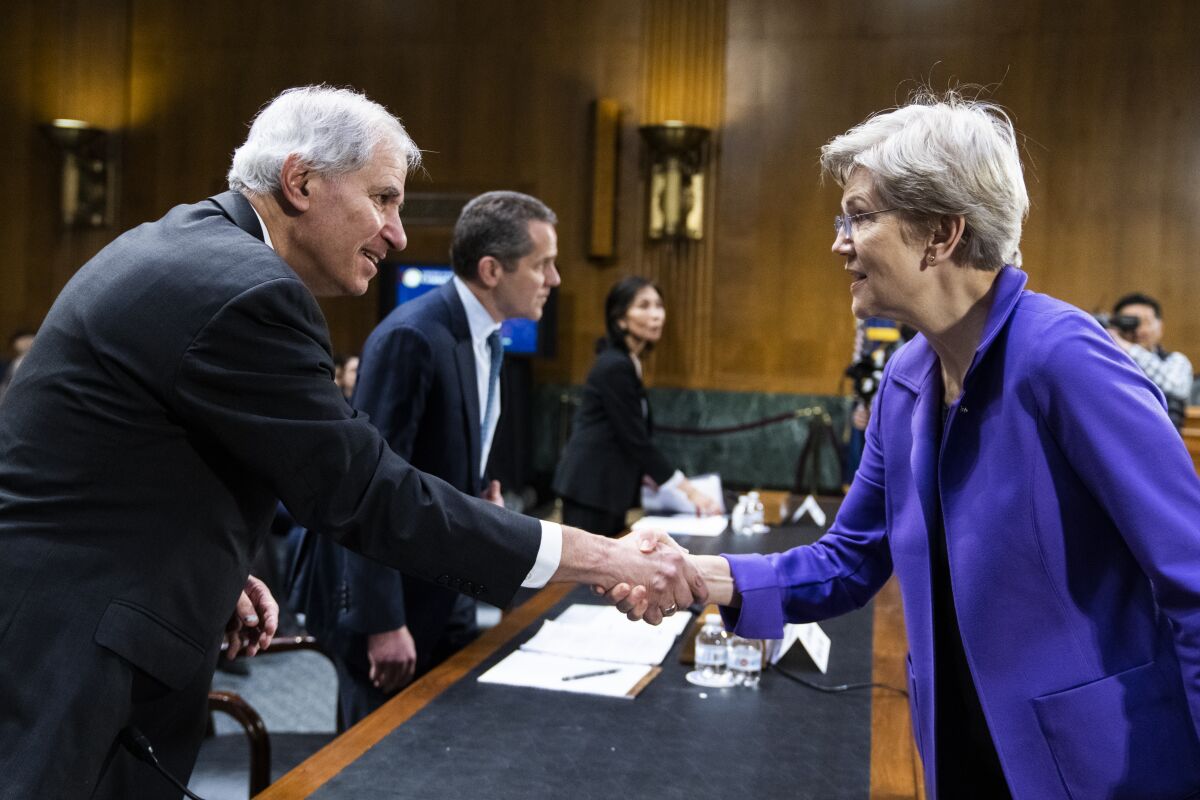 A woman shakes hands with a man across a desk.