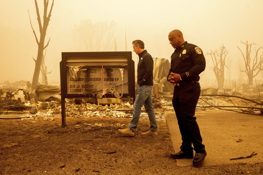 FILE - California Gov. Gavin Newsom examines a church marquee while visiting Greenville, which suffered extensive structure loss during the Dixie Fire, on Aug. 7, 2021, in Plumas County, Calif. Accompanying him is Cal Fire Assistant Region Chief Curtis Brown. Democratic governors such as California's Newsom and Washington's Jay Inslee have been clear about their plans to boost spending on climate-related projects, including expanding access to electric vehicles and creating more storage for clean energies such as solar. (AP Photo/Noah Berger, File)