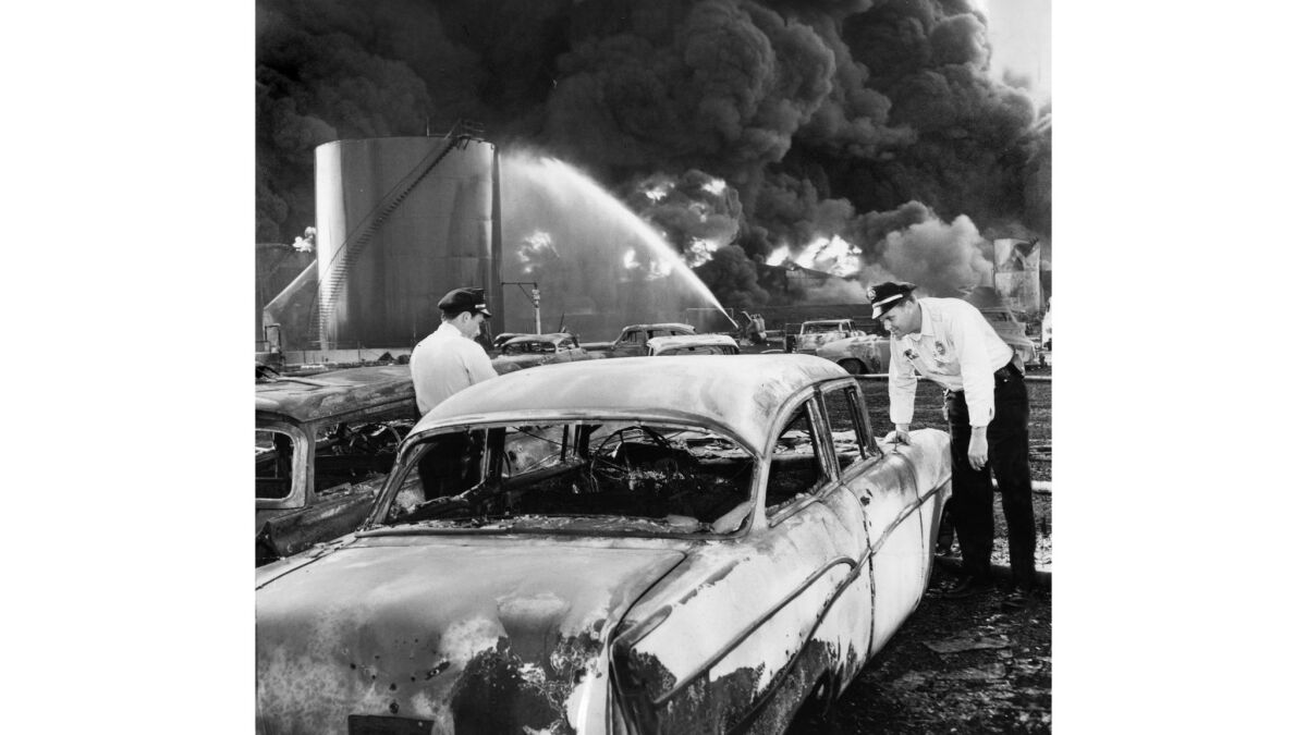May 23, 1958: Officers Tom Reynolds, left, and M. E. Yarbrough search one of the cars destroyed by fire as storage tanks at Hancock Oil Co., plant continue to burn in the background. This photo appeared in the May 24, 1958, Los Angeles Times.