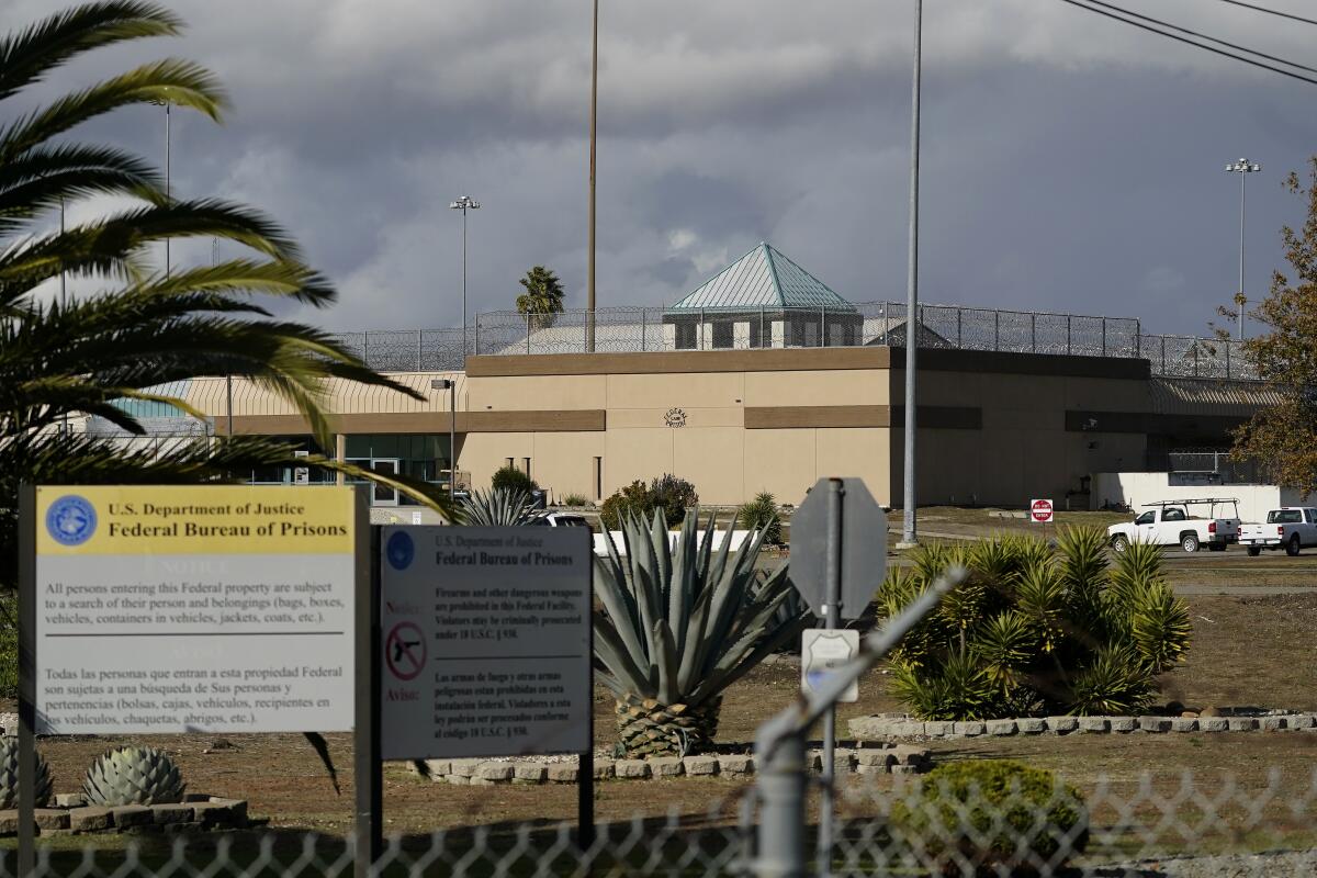 An exterior of a fenced building with tall walls and a sign that partially reads "Federal Bureau of Prisons."