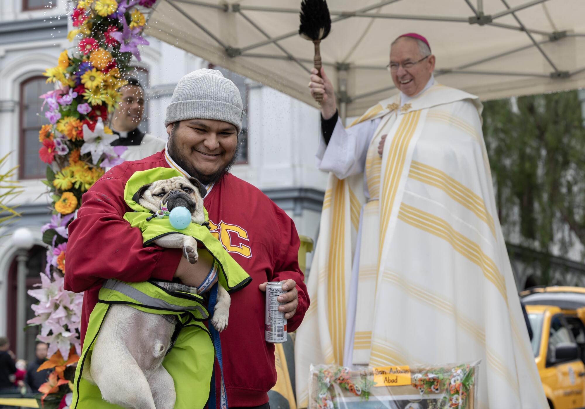 A man carries his dog as an archbishop looks on 