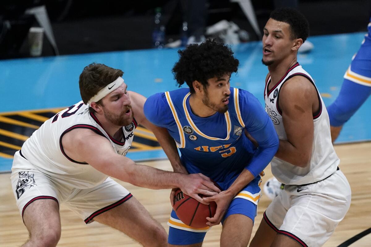 UCLA guard Johnny Juzang looks to pass between Gonzaga forward Drew Timme, left, and guard Jalen Suggs.