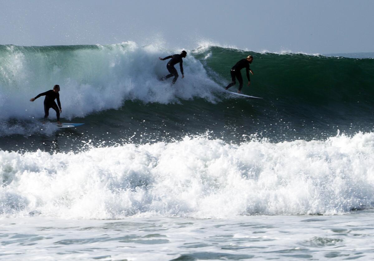 Three surfers take off on a monster wave off Newport Beach.