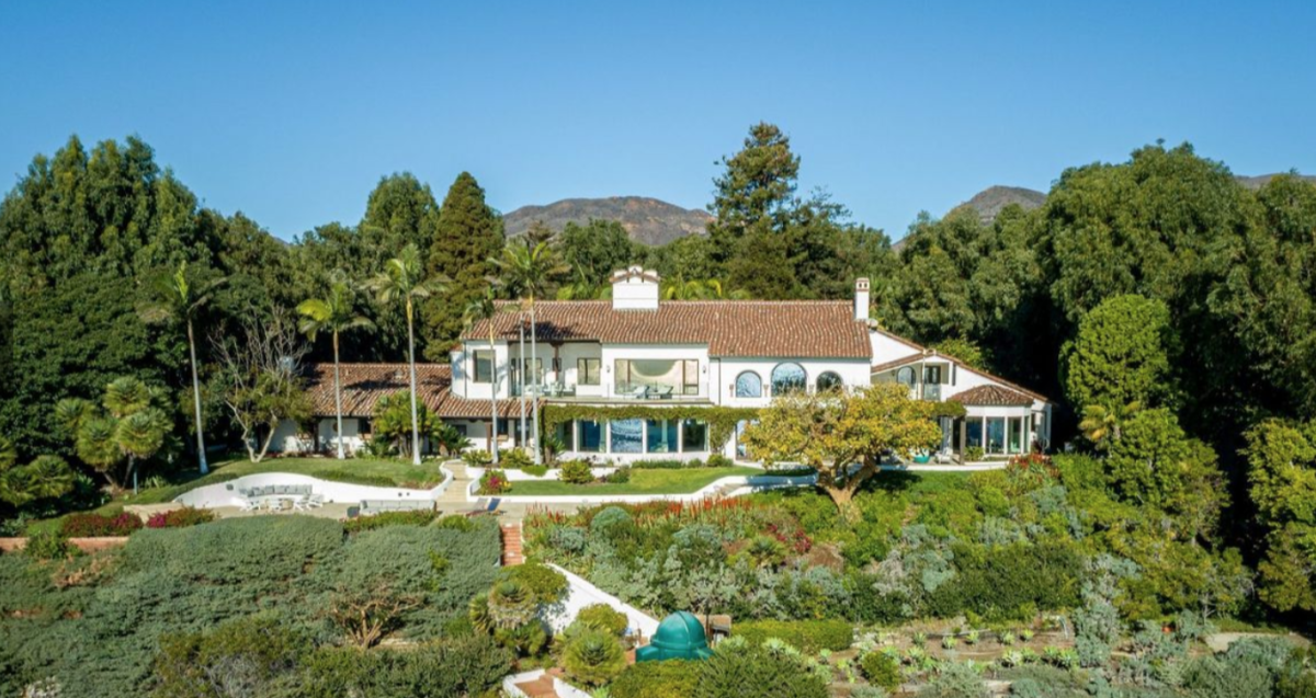 The mansion surrounded by trees, bushes and lawn.