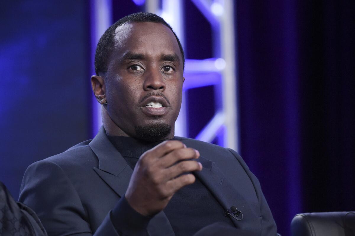 Sean 'Diddy' Combs motioning with his right hand while seated wearing a dark suit and black mock turtleneck
