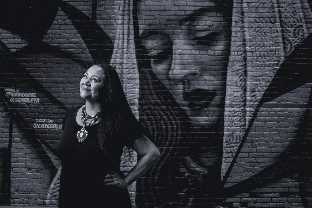 A woman stands in front of a painting on a brick wall