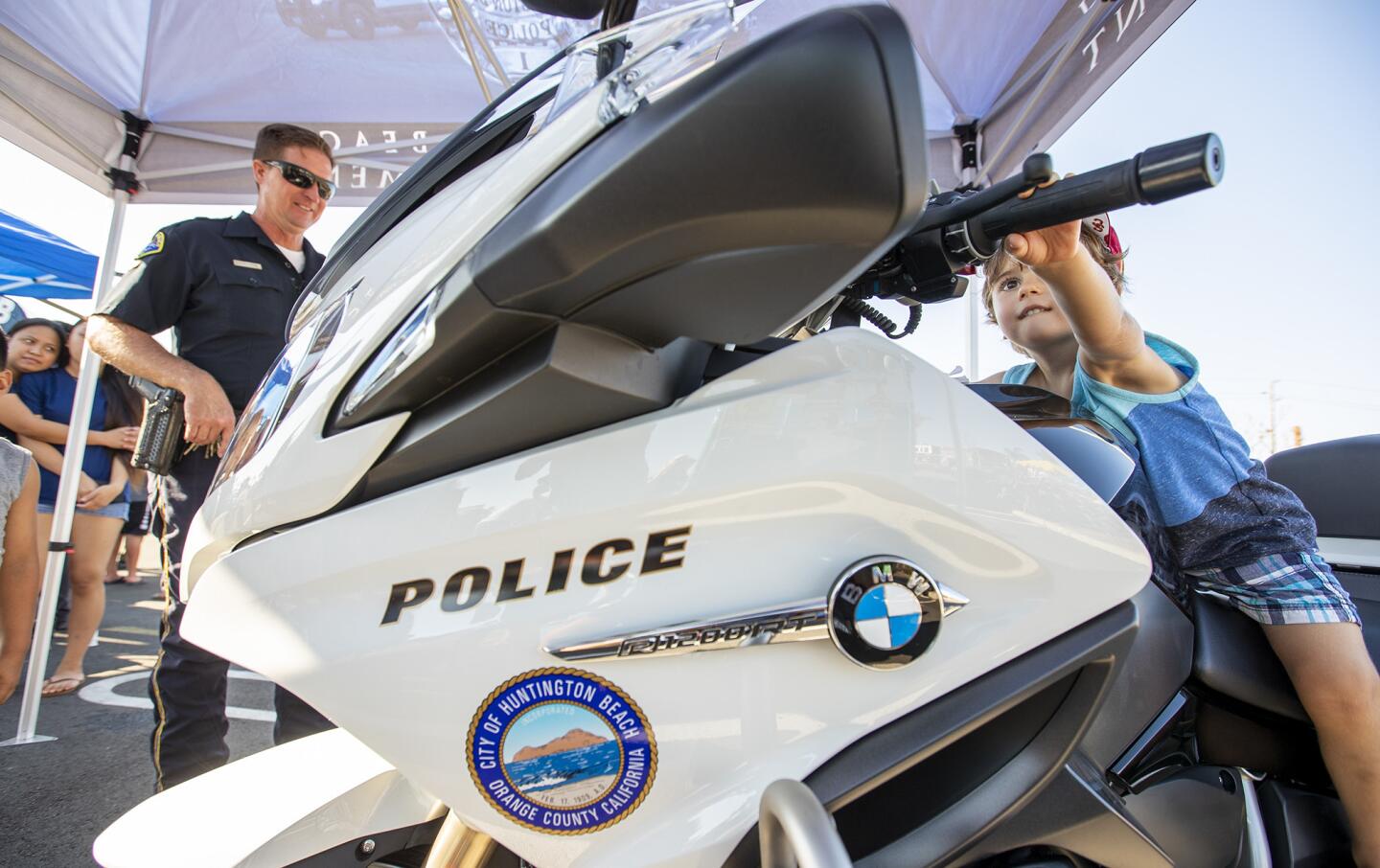 Huntington Beach Police Officer Bobby Frahm looks on as Levi Bonjean, 2, sits on his motorcycle. The Huntington Beach police and fire departments participate in the National Night Out event at the Target shopping center at Adams Avenue and Brookhurst Street on Tuesday, August 7.