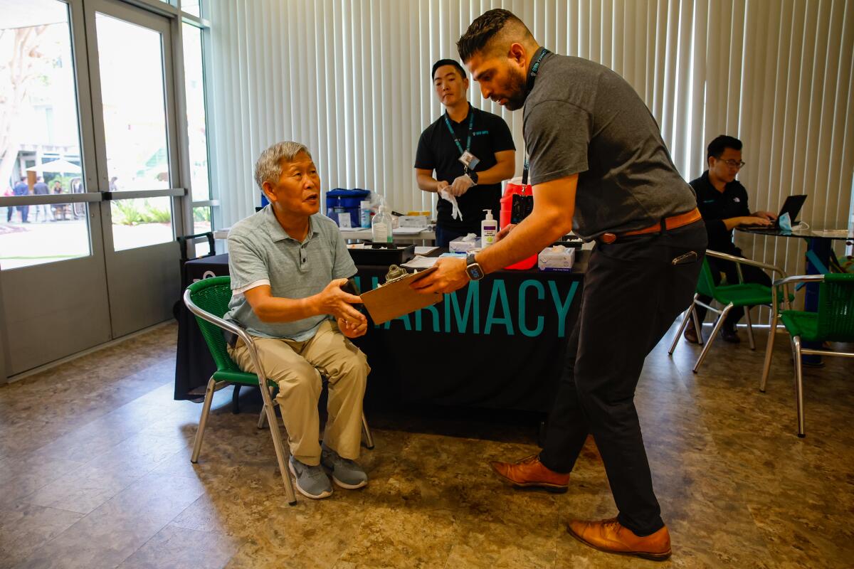 A man sitting in a chair is handed a clipboard by another man standing next to him.