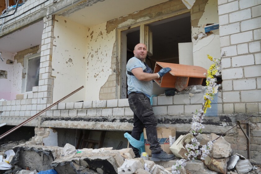 Un homme tire une étagère à travers une fenêtre d'un immeuble bombardé.