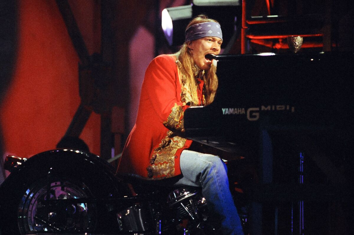A long-haired man with a bandanna on his head plays the piano.