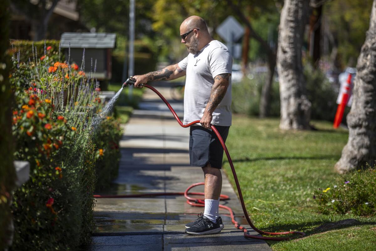A man waters flowers in his front yard.