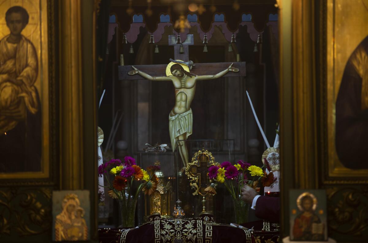 A painting of a crucifixion rises over an altar bearing icons and bundles of flowers inside a 12th century church