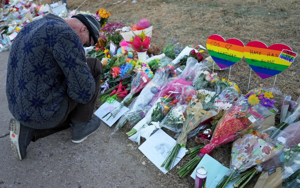 A man prays at a makeshift tribute with a display of bouquets of flowers.