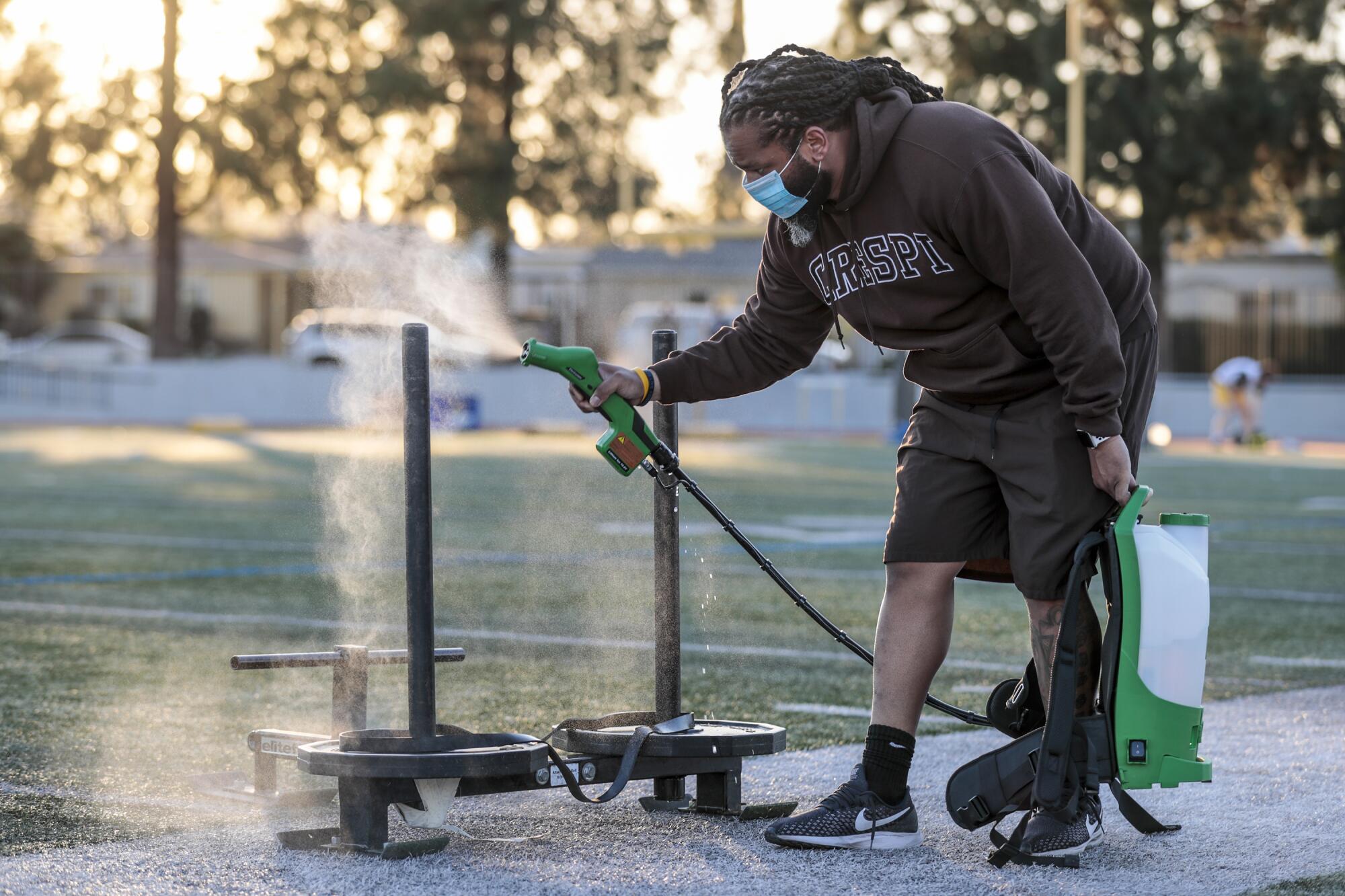 Coach Benjamin Oyeka disinfects weight sleds at Crespi High.