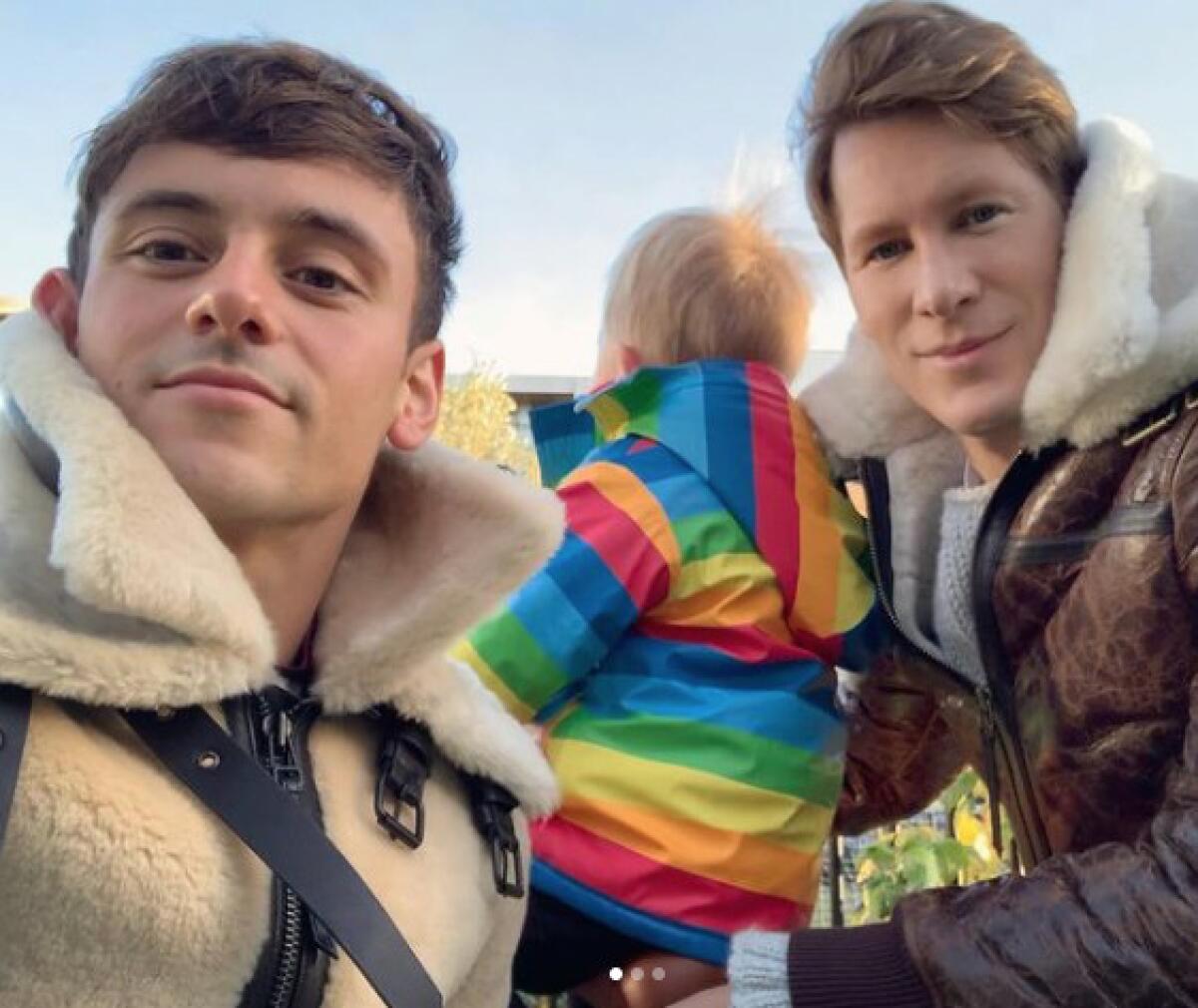 Two men with their baby, who is dressed in a rainbow pattern jacket