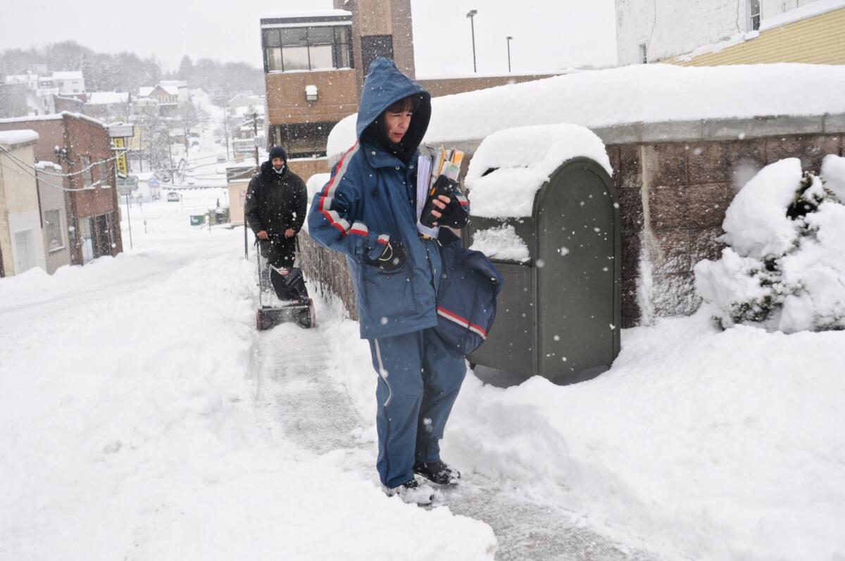 U.S. Postal Service mail carrier Debra Zyk delivers mail on her route in Pottsville, Pa., as Sebastian Lopez clears snow.