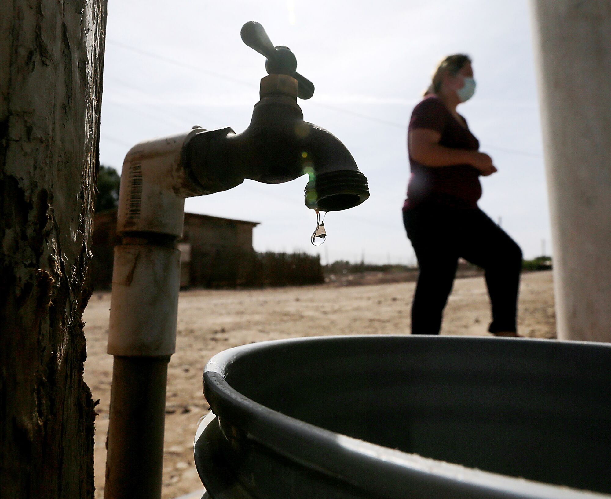 Water drips out of a faucet into a bucket as a person walks behind