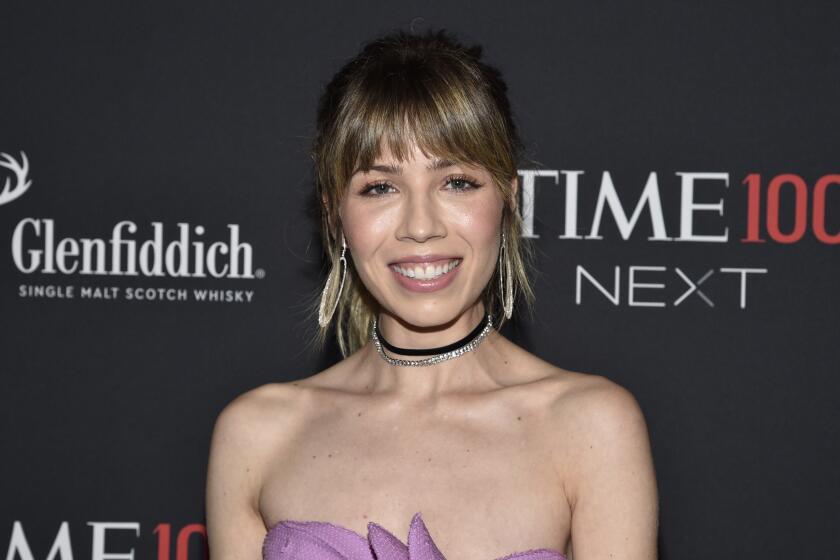 Jennette McCurdy smiles while wearing a sparkly choker and purple dress against a black background.