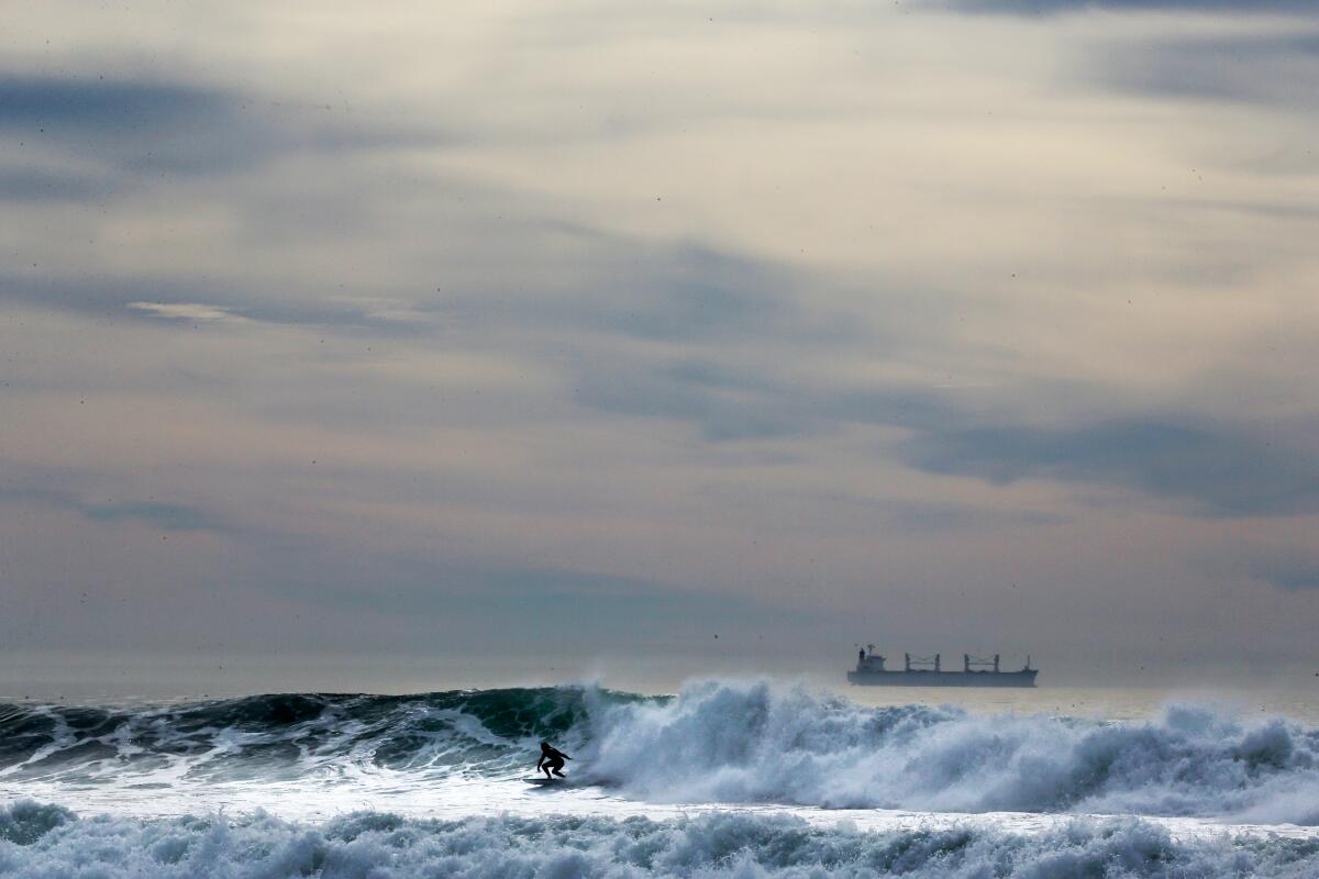 A surfer rides a wave. A ship is in the background.