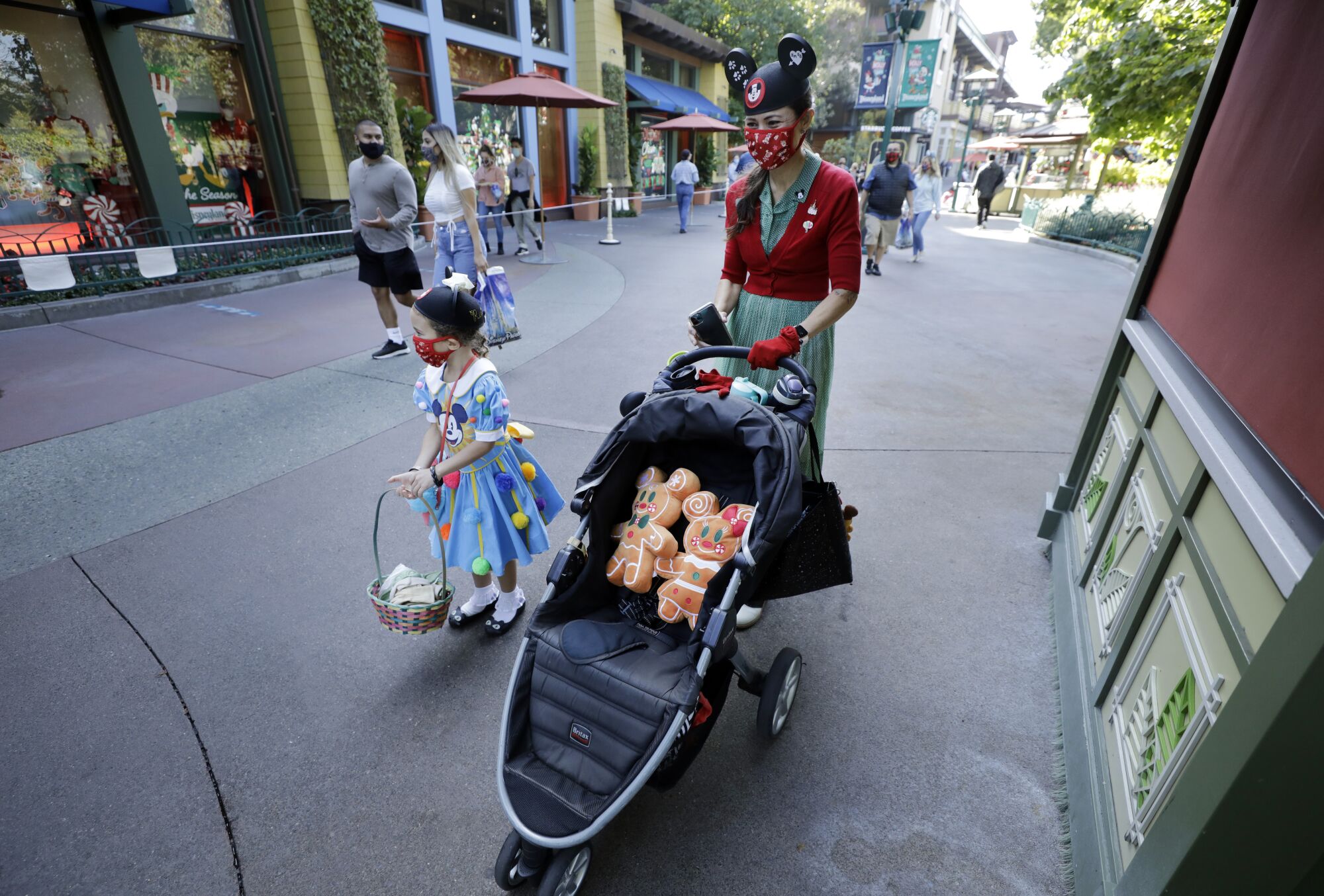 A woman in Minnie Mouse ears pushes a stroller while her daughter in a Disney dress walks next to her